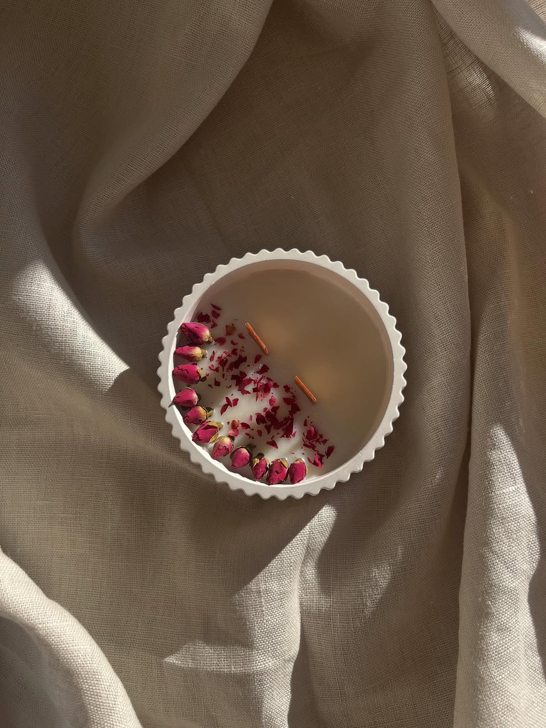 Handmade soy candle decorated with dried roses on warm linen